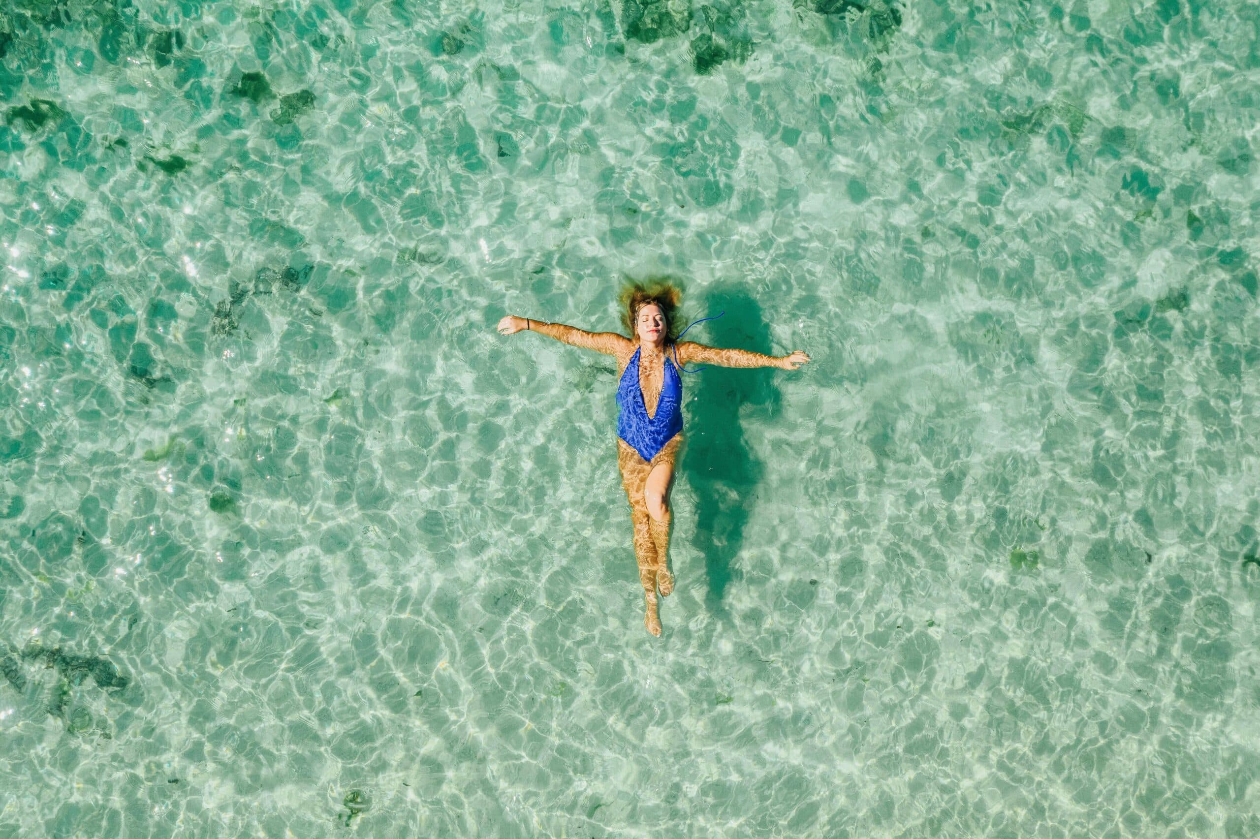 Tranquilidade, segurança, paz: mulher deitada no mar de água calma e transparente
