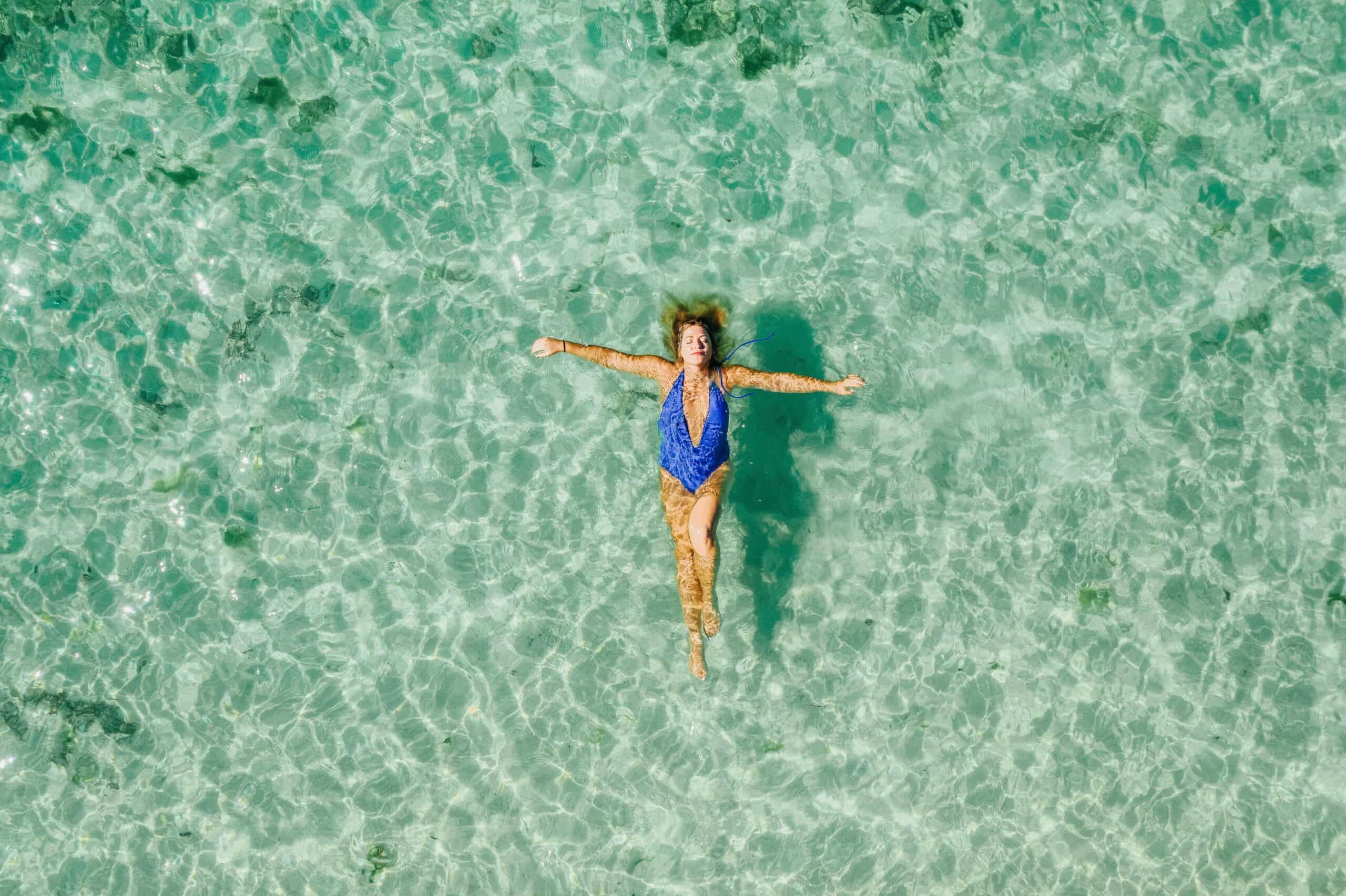 Tranquilidade, segurança, paz: mulher deitada no mar de água calma e transparente